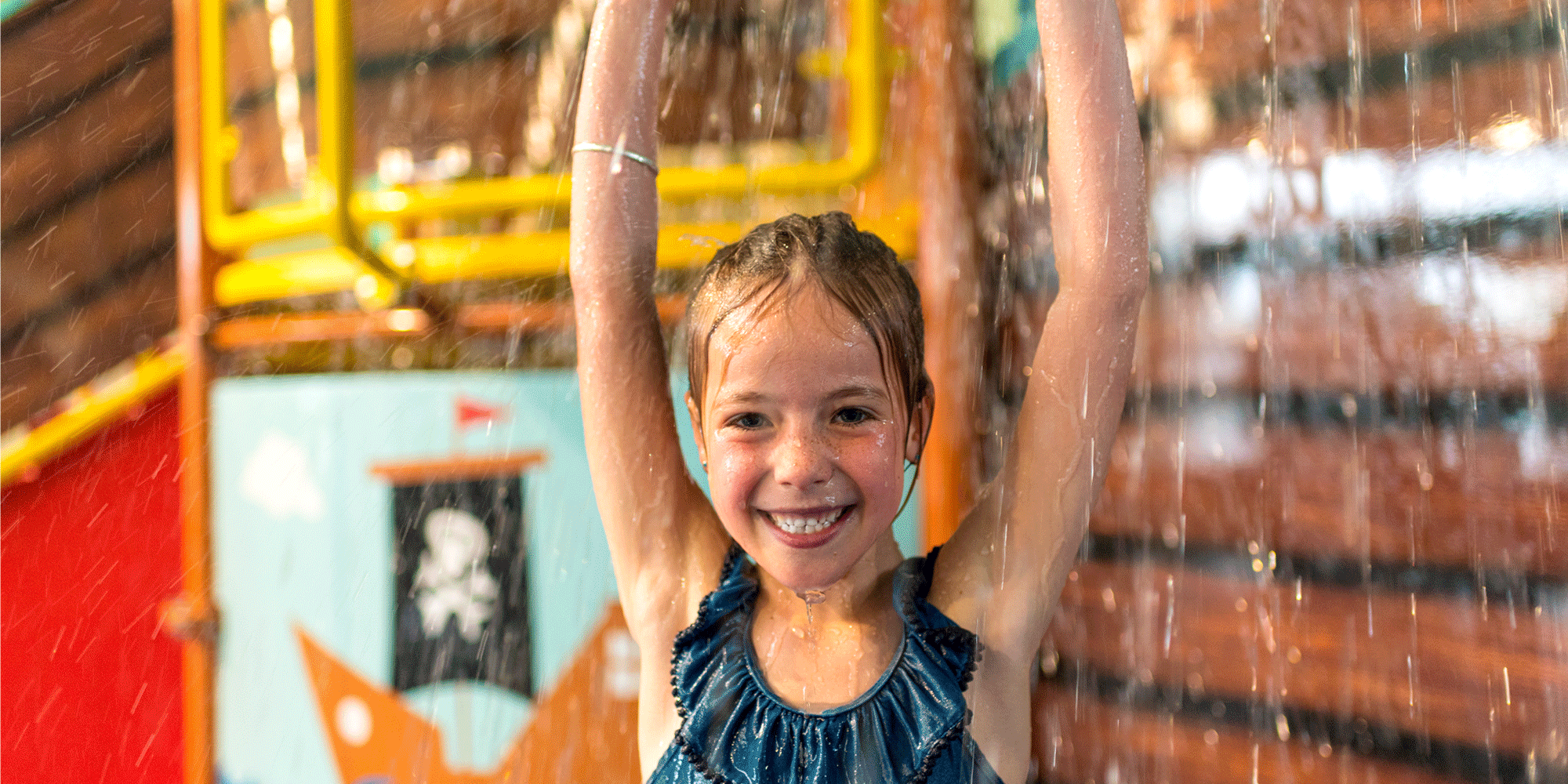 Girl standing under aqua play station fountain and smiling
